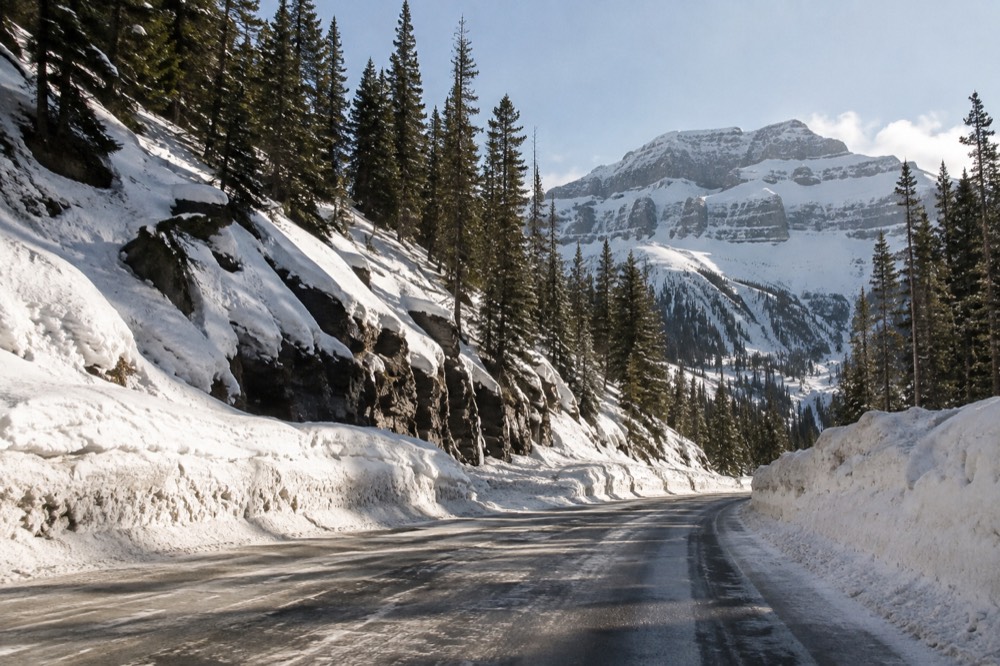 A snow-covered mountain road with winter trees under a clear sky