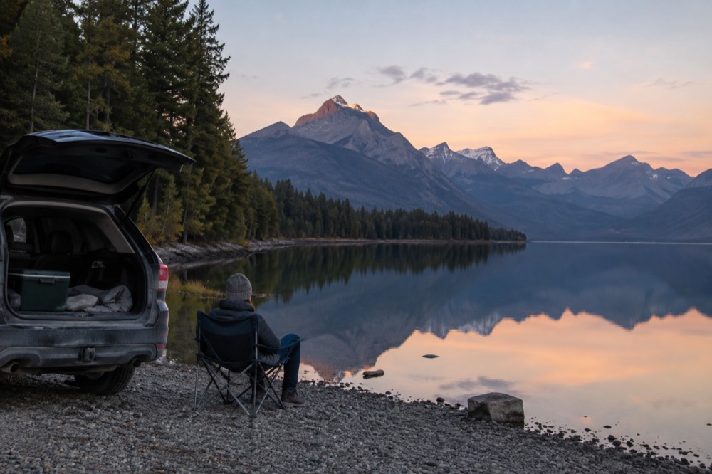 A family vehicle parked at a lakeside viewpoint with mountains reflected in still water
