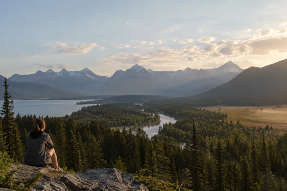 A wide valley with a winding river and forested slopes beneath distant snowcapped mountains