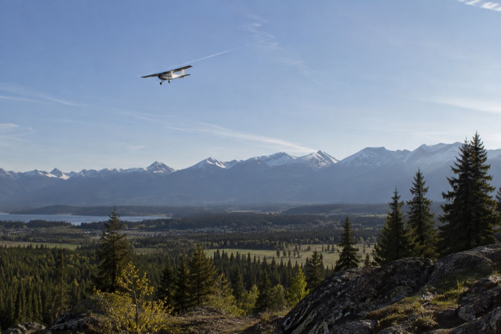 A small aircraft flying above a broad forested valley with mountains on the horizon