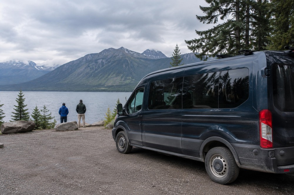 A guided tour vehicle stopped at a lakeside viewpoint with forested mountains behind