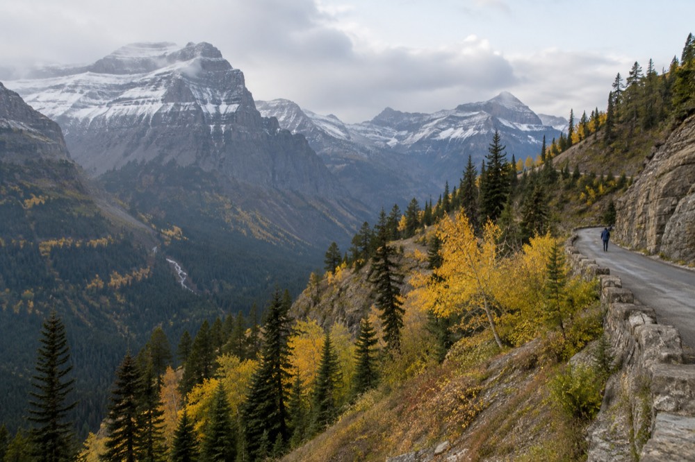 A mountain road in early autumn with golden trees on the slopes and dusting of snow on high peaks