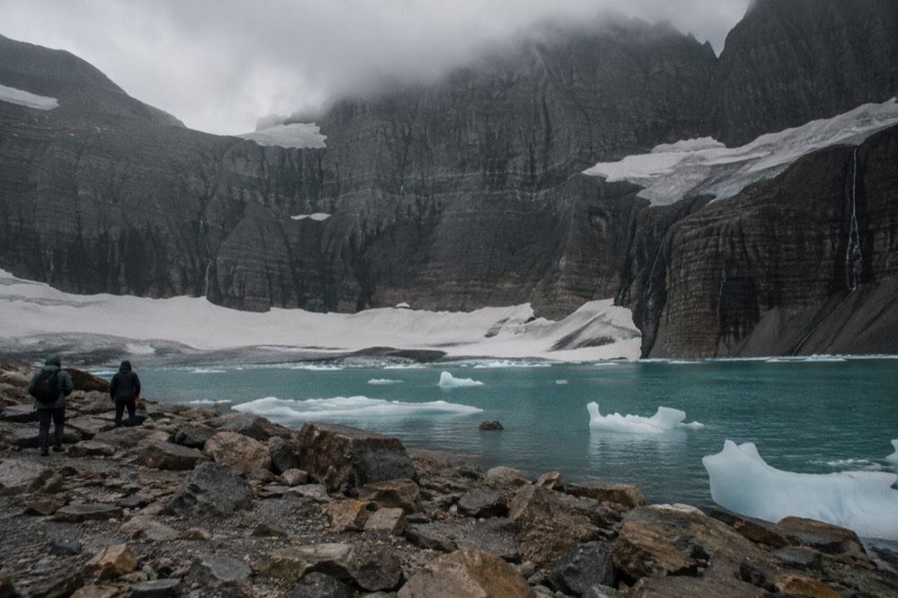 A turquoise alpine lake sitting below steep rock walls under scattered clouds