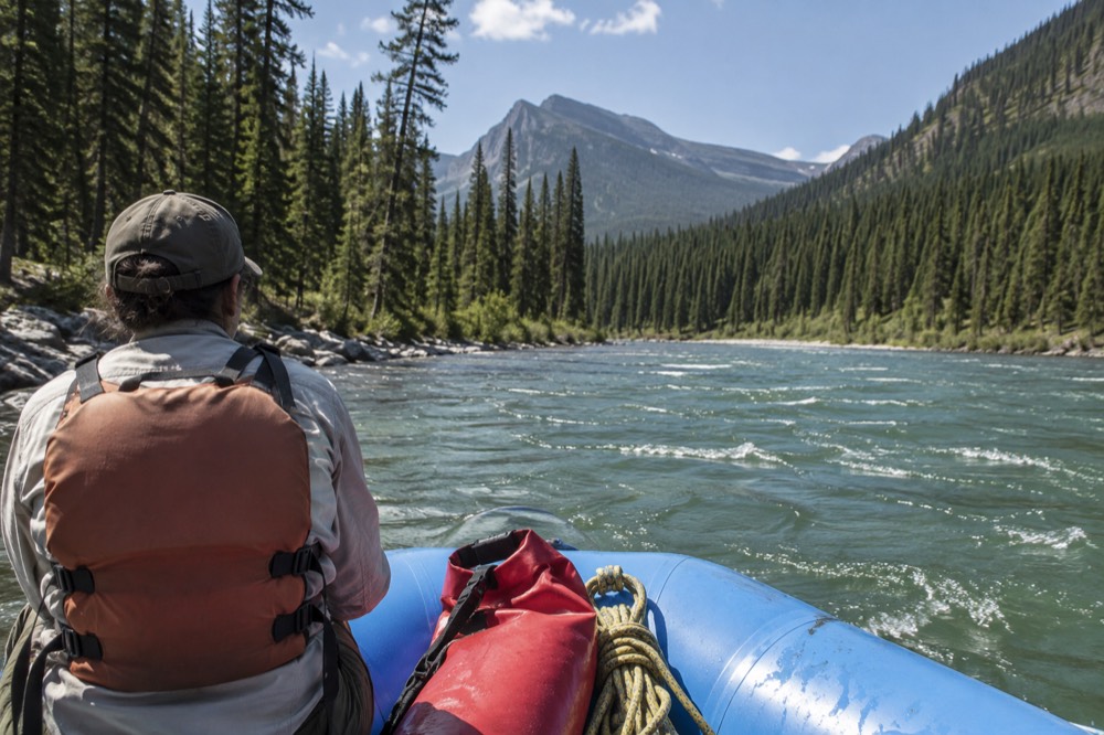 A raft floating on wide green water between forested banks and mountain ridges
