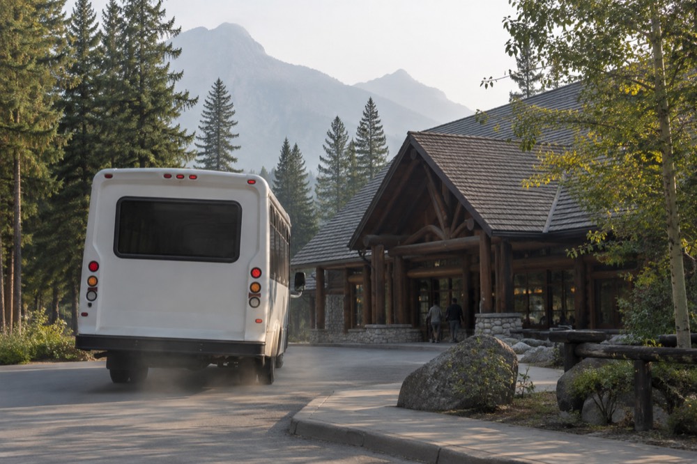 A shuttle bus pulling away from a curb beside a visitor center parking area