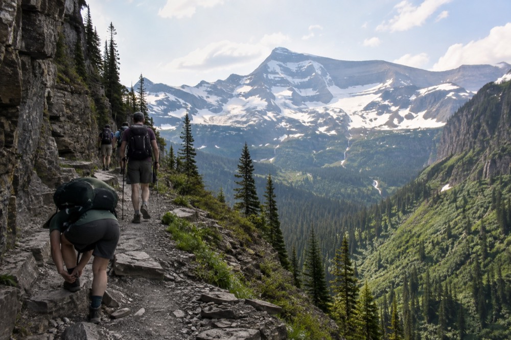 A group of hikers walking a trail toward a snow capped mountain ridge