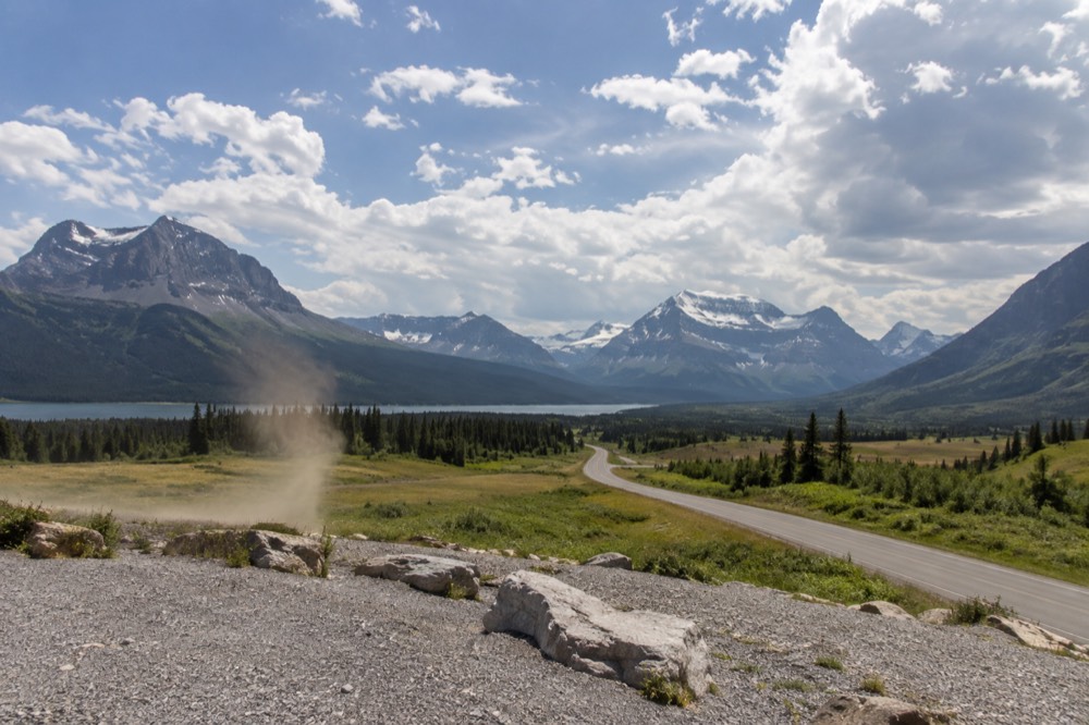 An open road curving toward distant snow capped mountains under a wide sky