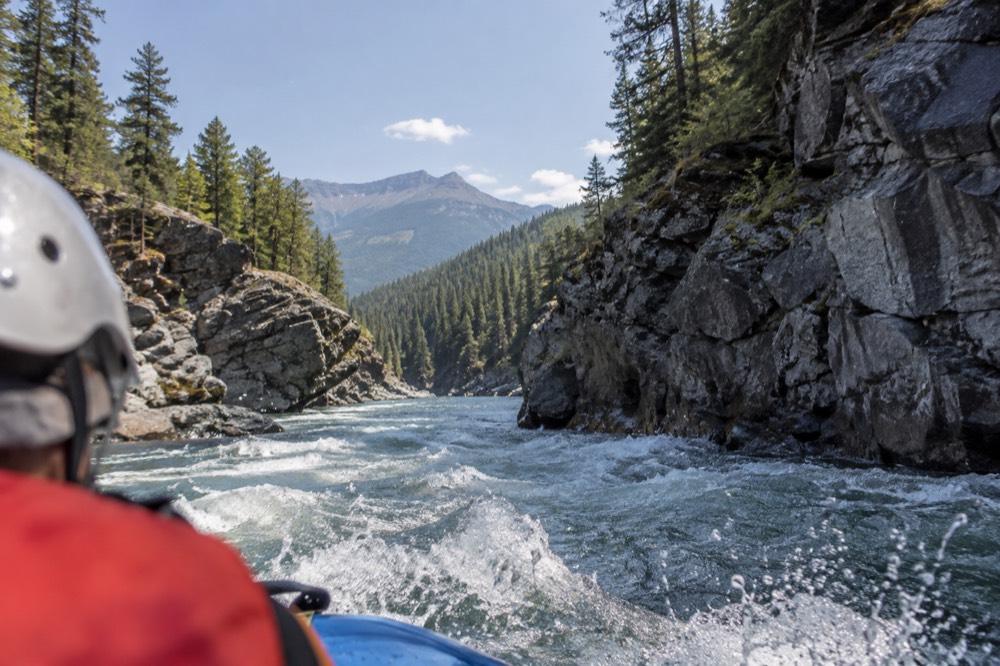 A raft passing between rock walls on a forested river canyon