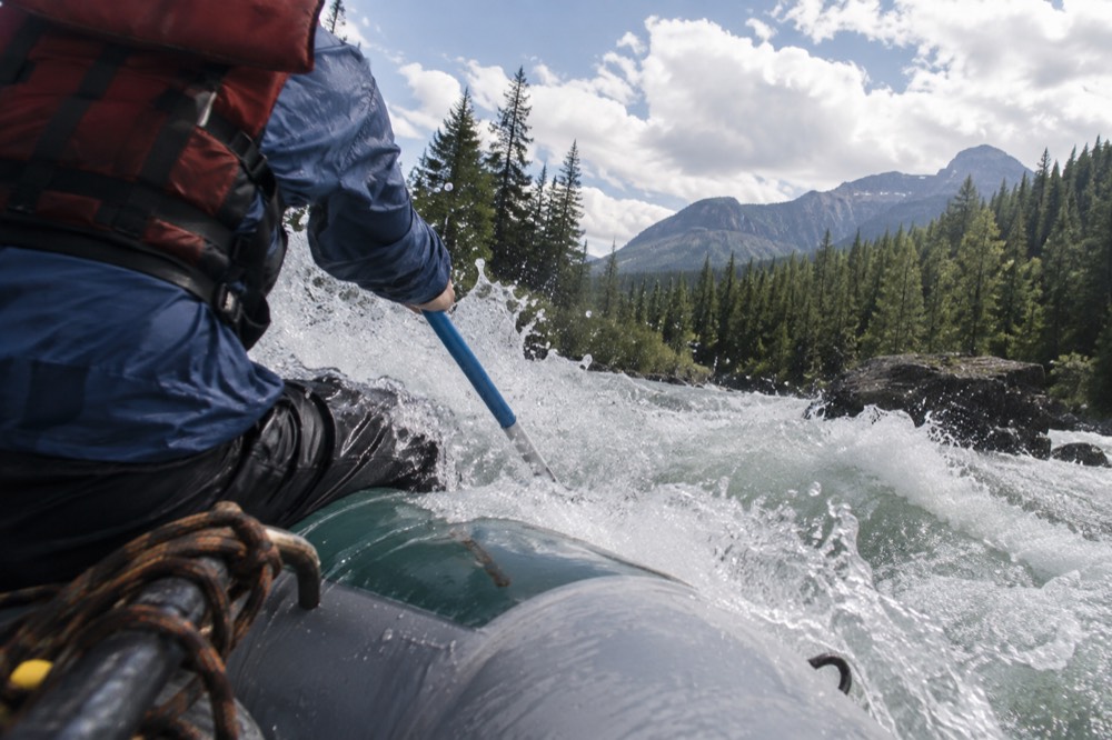 A guide paddling a raft through a standing wave