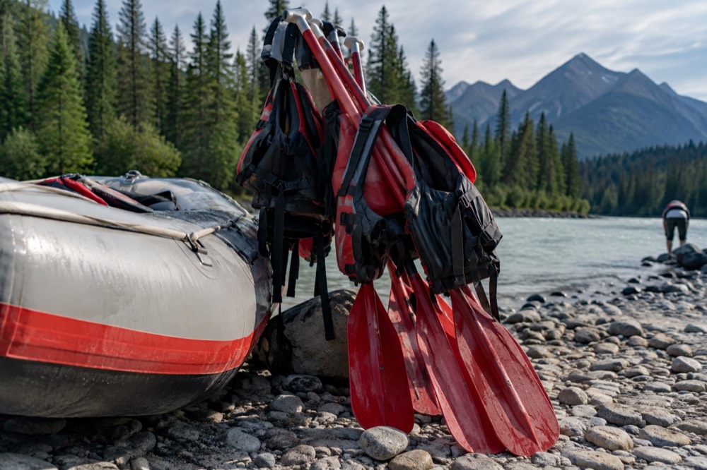 A stack of paddles and life jackets on a riverbank beside a raft