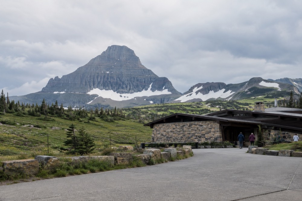 Logan Pass visitor center parking area with mountains rising above the alpine meadow
