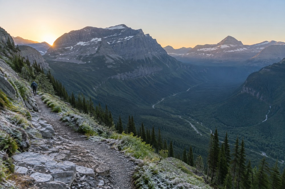 A hiker's viewpoint over a green alpine valley with a winding road far below