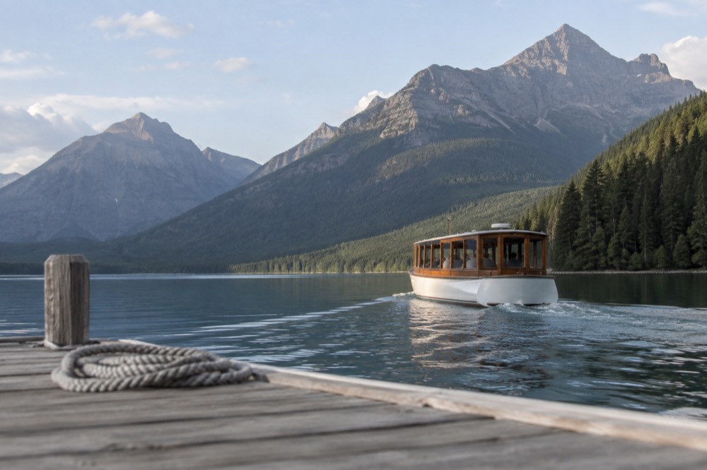 A wooden tour boat crossing a still mountain lake toward forested slopes