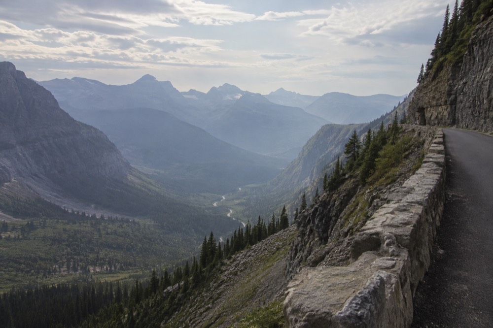 A narrow mountain road curving along a cliff face with a valley far below