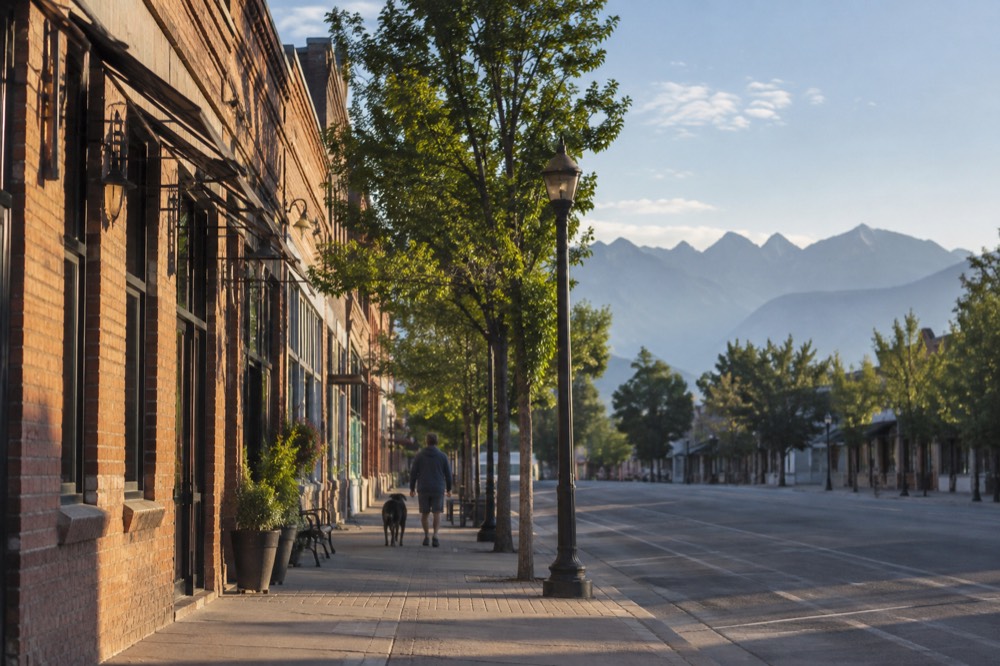 A small city street with mountains visible in the distance under a wide sky