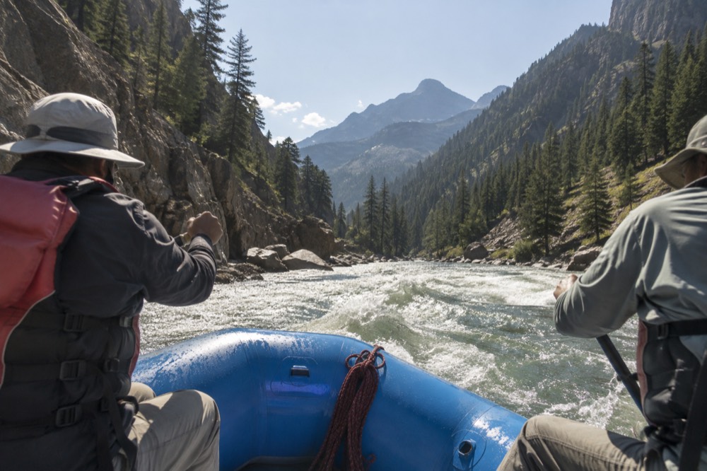 A raft passing through a rocky river canyon with forested slopes