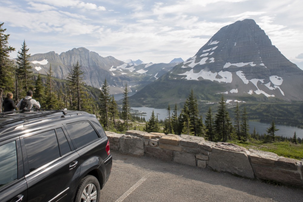 A large SUV parked at a scenic overlook with a valley and mountains beyond