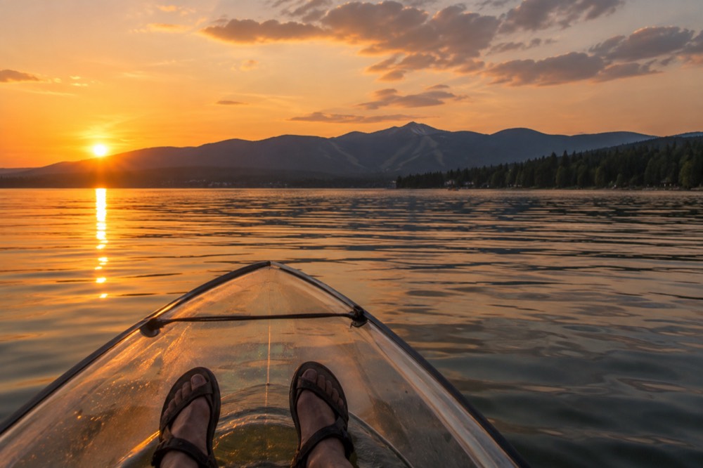 A clear bottom kayak on a calm lake at sunset with mountains on the horizon