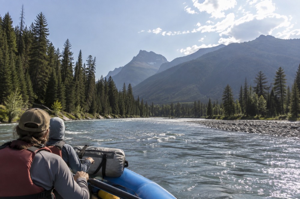 A raft floating on a wide river with forested mountains along the bank