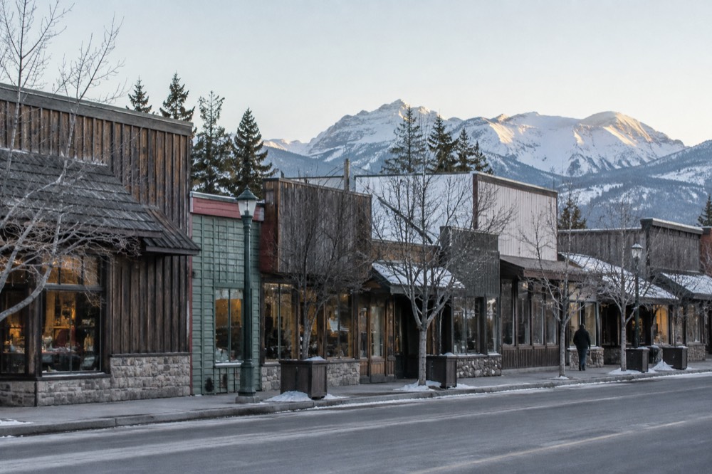 A small town street with wooden storefronts and mountains rising behind the rooftops