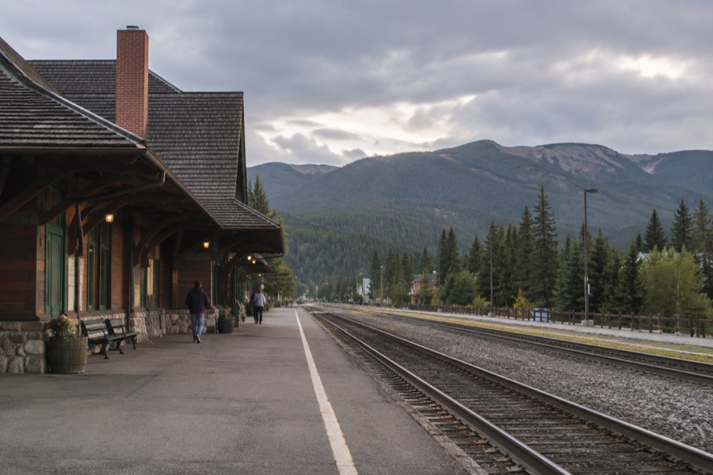 A train platform beside a wooden depot with forested hills in the background