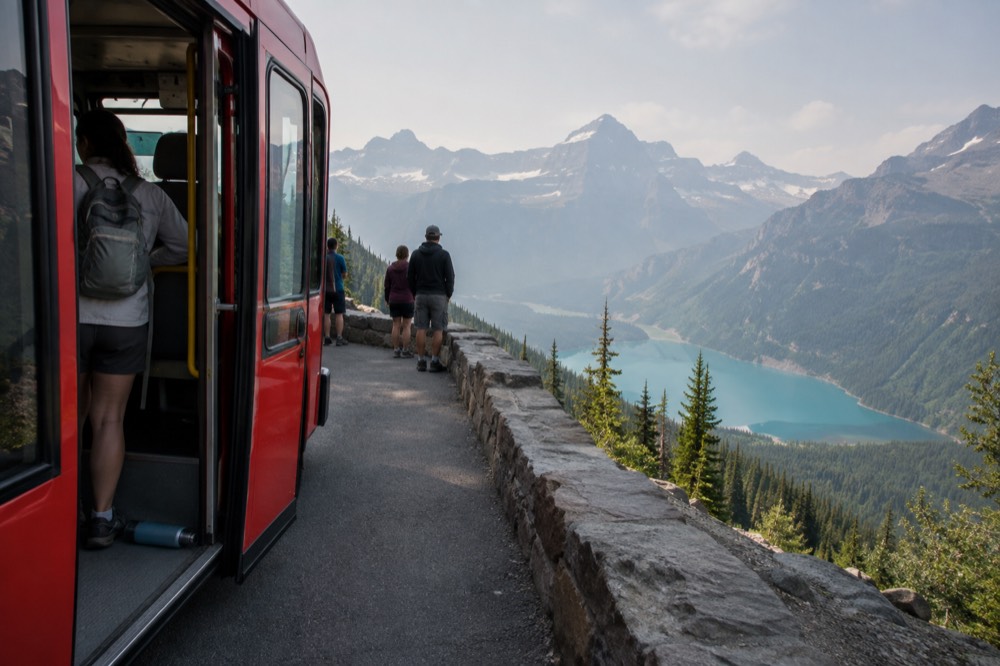 A red shuttle bus parked at a scenic overlook above a glacial lake
