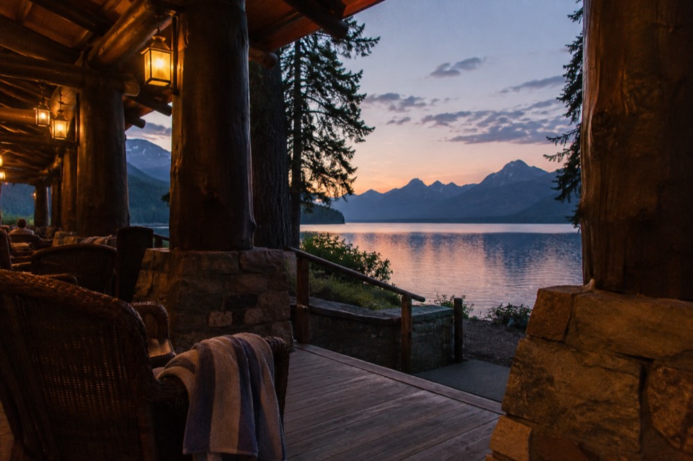 A wooden lodge porch overlooking a long glacial lake at dusk