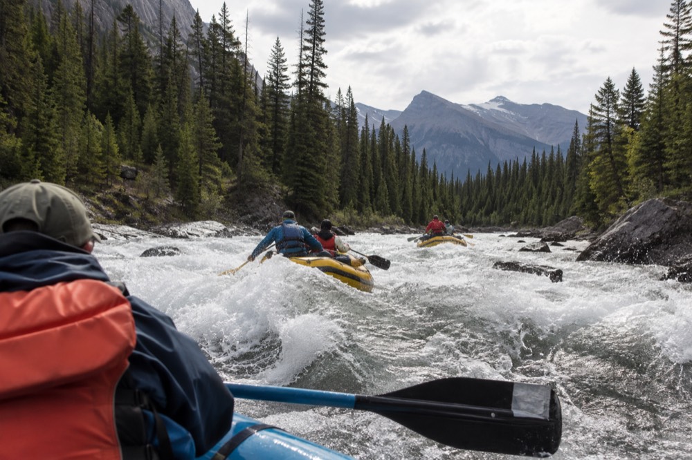 Whitewater rafts passing through a rocky rapid on a forested river