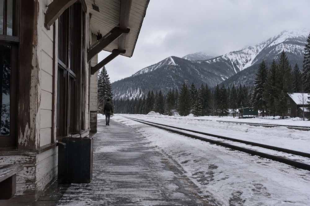 A train depot platform in winter with snow on the rails and dark timber mountains behind