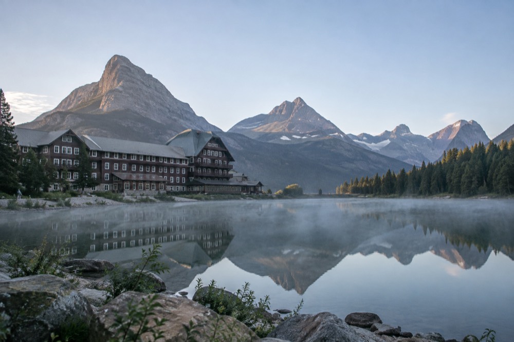 A historic log hotel beside a calm lake with mountains reflected in the water