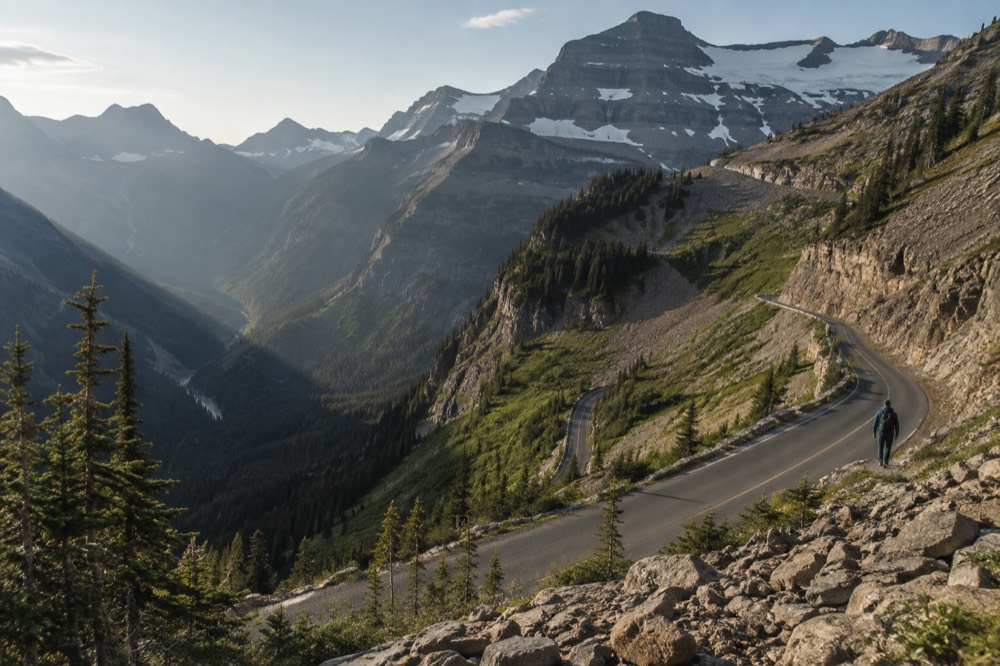 A winding mountain road climbing toward a snowy ridgeline above treeline