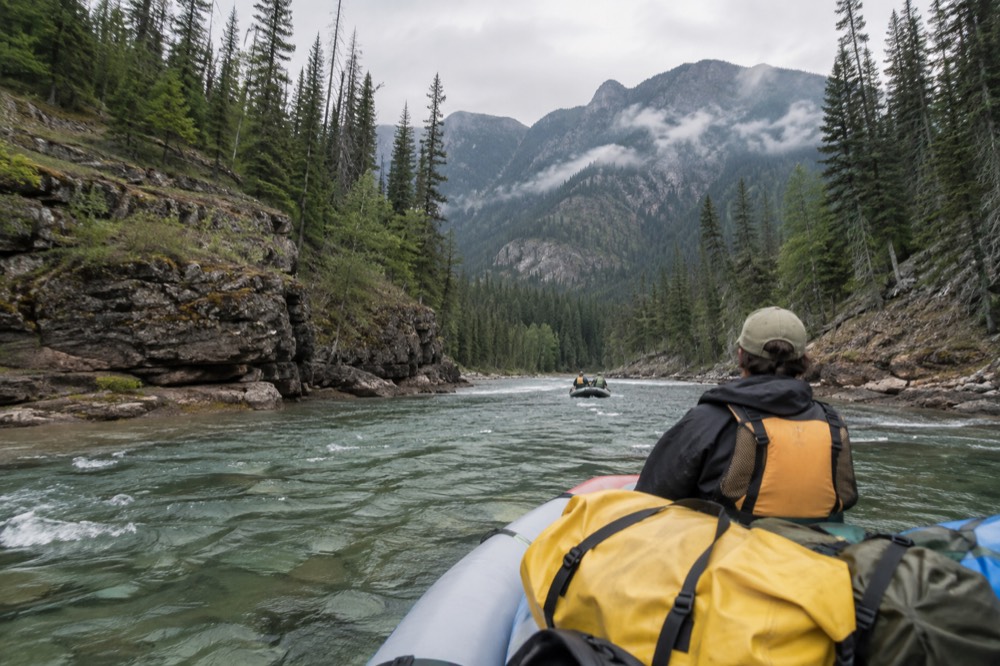 A raft floating through a forested river canyon with clear green water