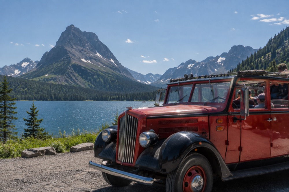 A vintage open-top tour bus parked beside an alpine lake