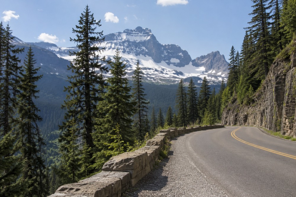 A winding mountain road climbing through forest toward snow-capped ridges