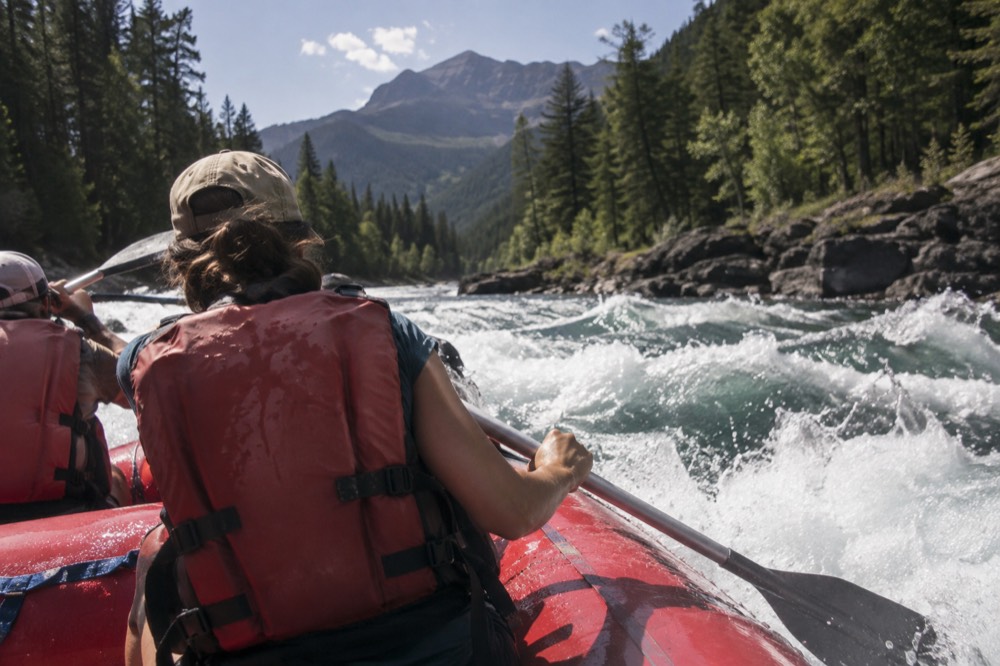 A raft cutting through whitewater on a forested river in summer