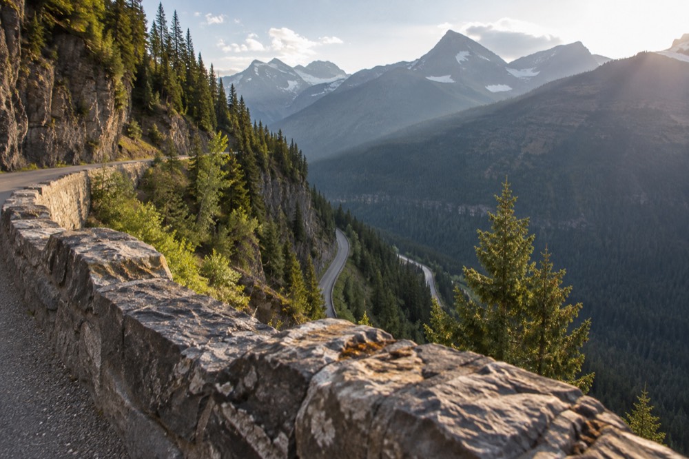 A steep winding road descending a mountainside with a stone guardrail