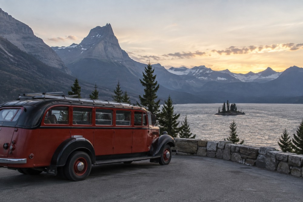 A red historic touring bus parked at a viewpoint above a glacial lake
