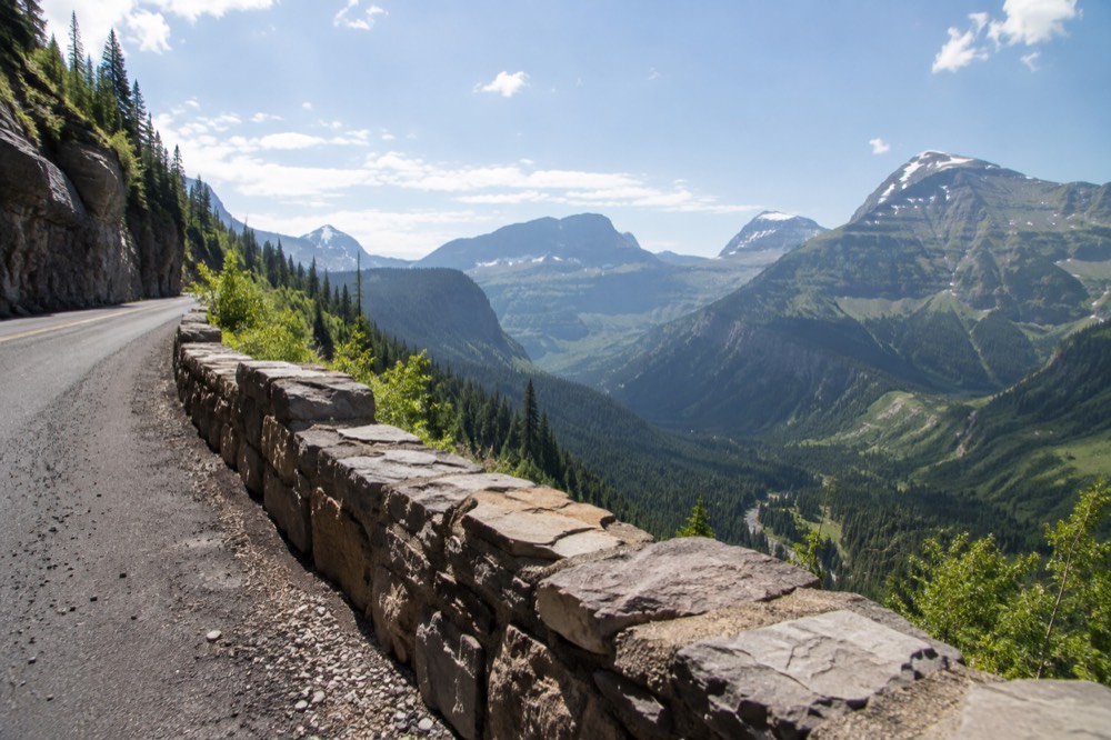 A mountain road hugging a cliff face above a green valley