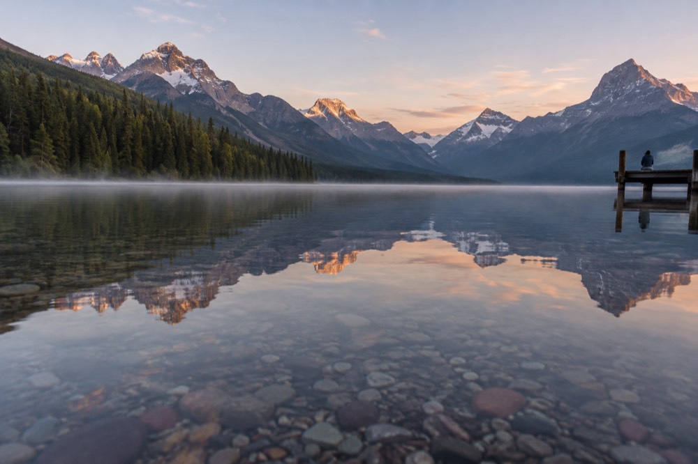 A calm mountain lake reflecting tall peaks in early morning light