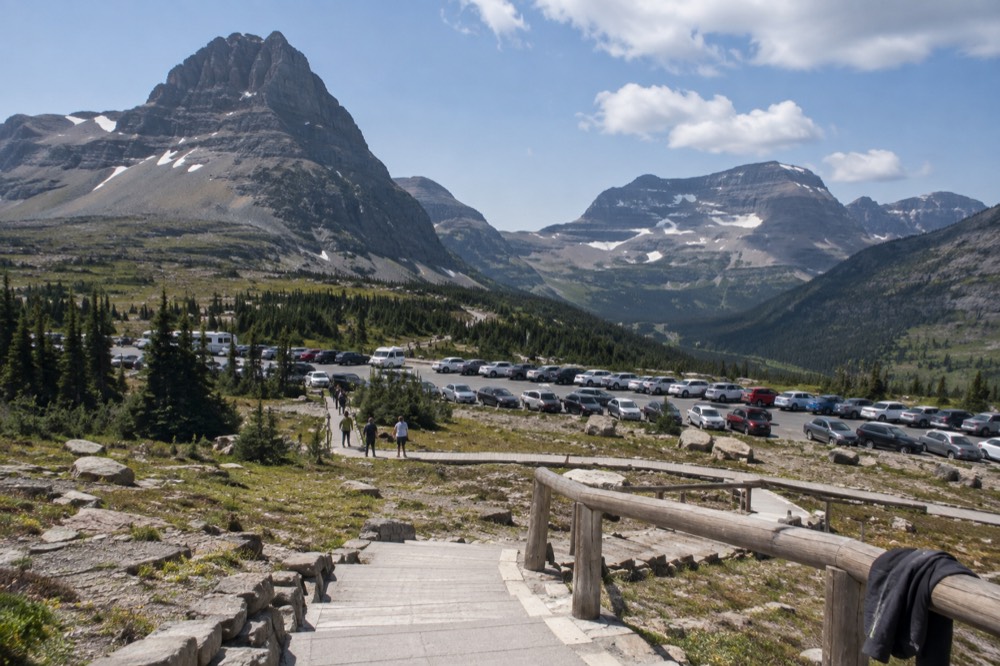 A filled gravel parking lot beneath a rocky alpine pass with boardwalk trails