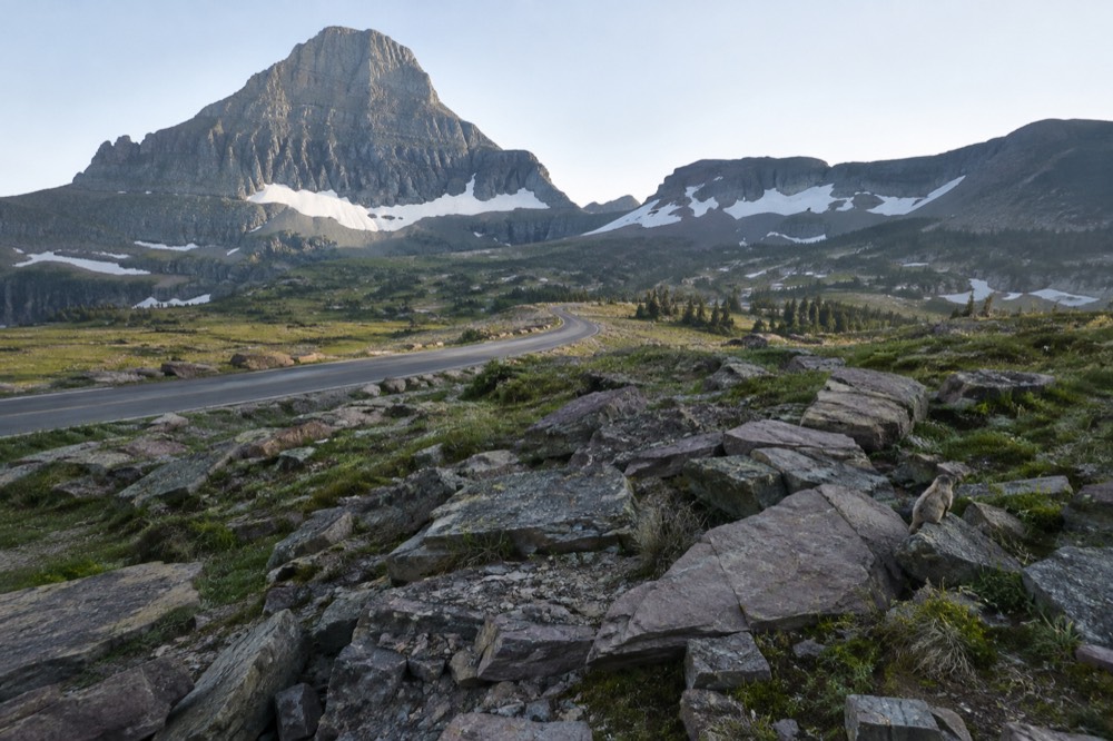 A long alpine road winding toward a snow dotted mountain pass