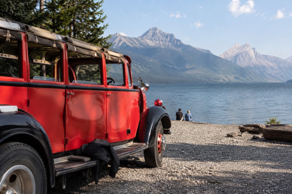 A red vintage tour bus parked beside an alpine lake