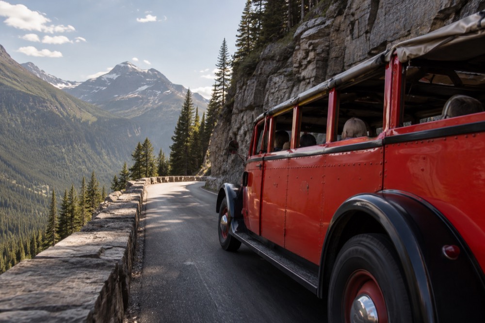 A vintage red touring bus with an open canvas top driving along a mountain road