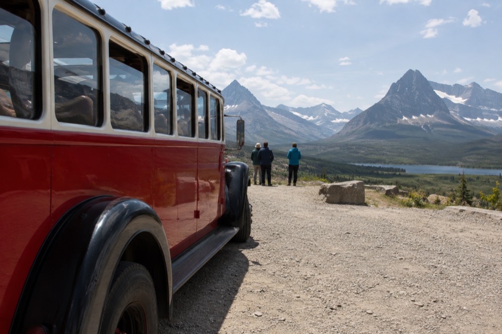 A red jammer bus parked at a scenic overlook with a valley and distant peaks beyond