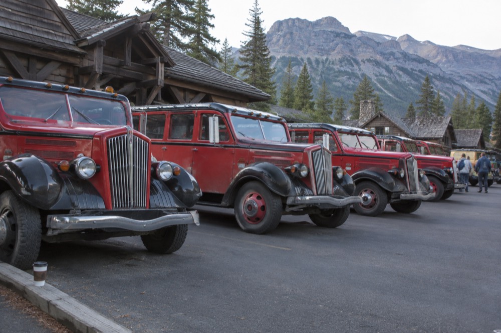 A parking lot with red buses lined up near a wooden village storefront