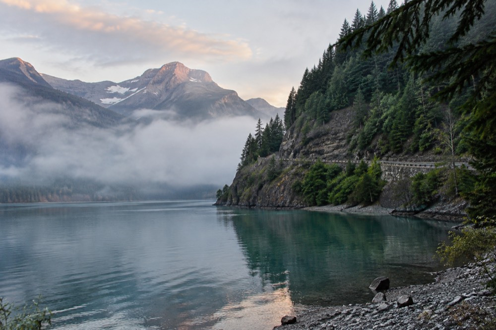 A scenic mountain road curving along a cliff face above a glacial lake