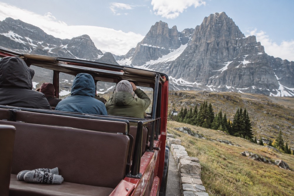 A red bus with its canvas top rolled back and passengers looking up at cliffs