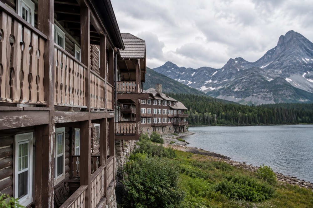 Many Glacier Hotel on the shore of Swiftcurrent Lake with mountain peaks in the background.